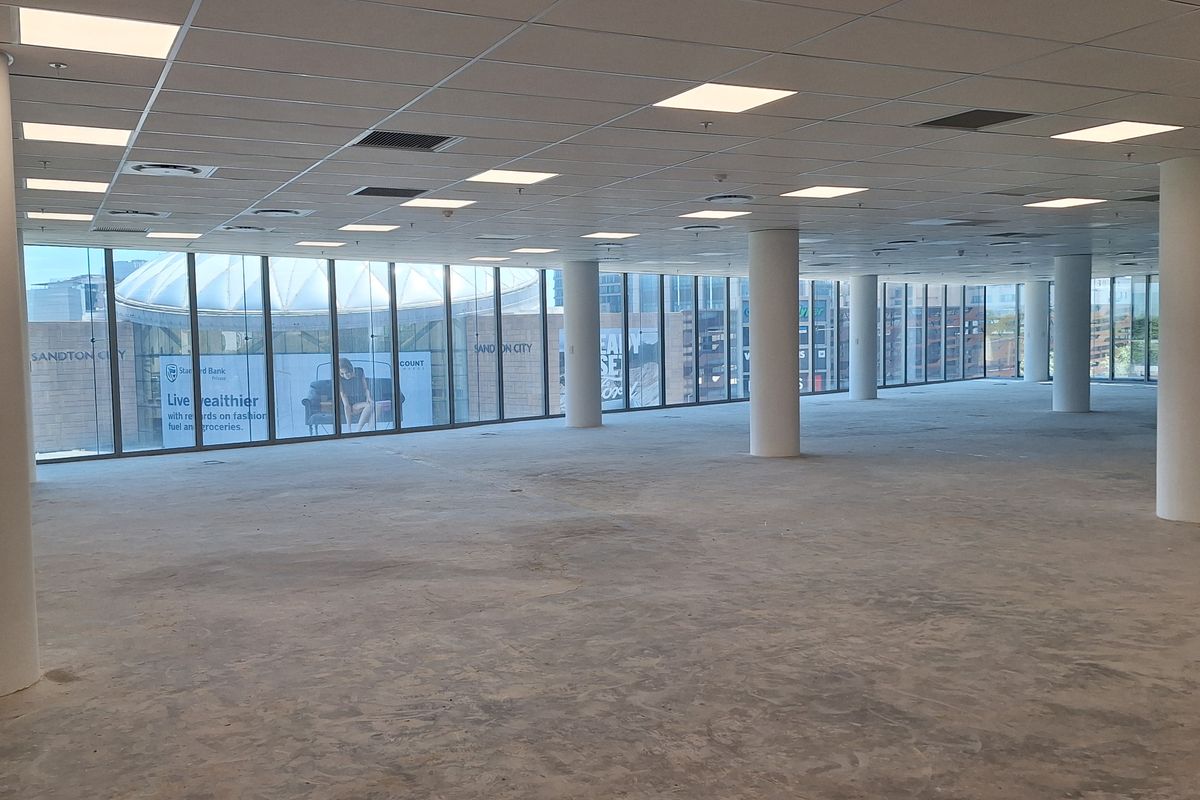 Spacious open-plan office area featuring floor-to-ceiling windows, suspended ceilings with recessed lighting, and structural columns, currently awaiting final flooring installation.