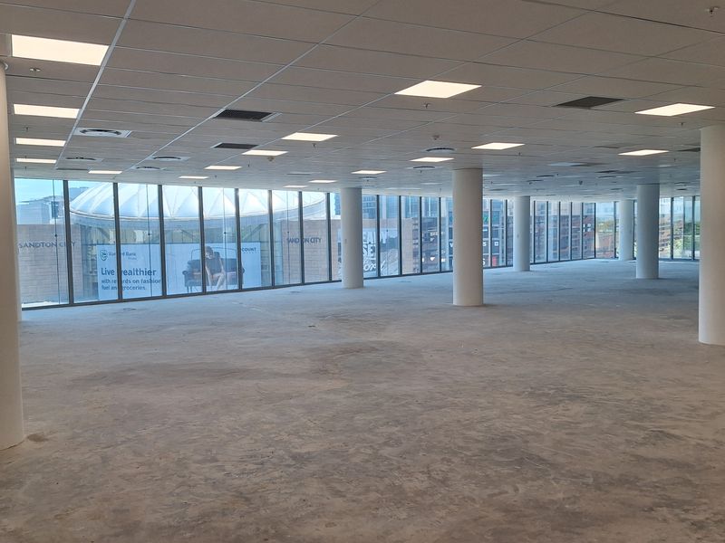 Spacious open-plan office area featuring floor-to-ceiling windows, suspended ceilings with recessed lighting, and structural columns, currently awaiting final flooring installation.