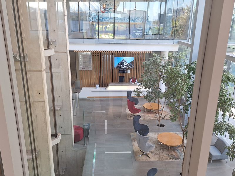 Modern office building atrium featuring a high-ceiling glass facade, reception area with timber detailing, and polished tiled flooring.