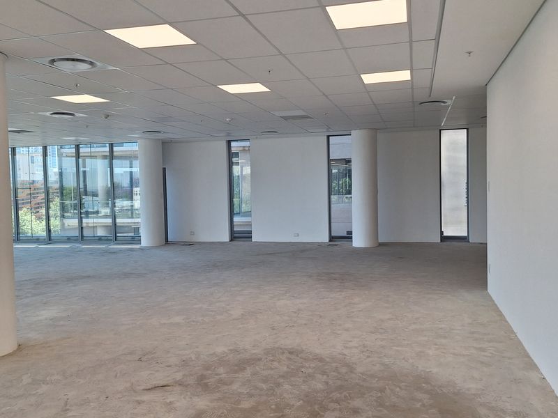 A spacious, open-plan office area featuring a suspended ceiling, recessed lighting, and large floor-to-ceiling windows providing ample natural light.