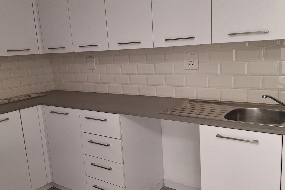 A clean, modern kitchen featuring white cabinetry, subway tile backsplash, grey stone countertops, and a stainless steel sink.