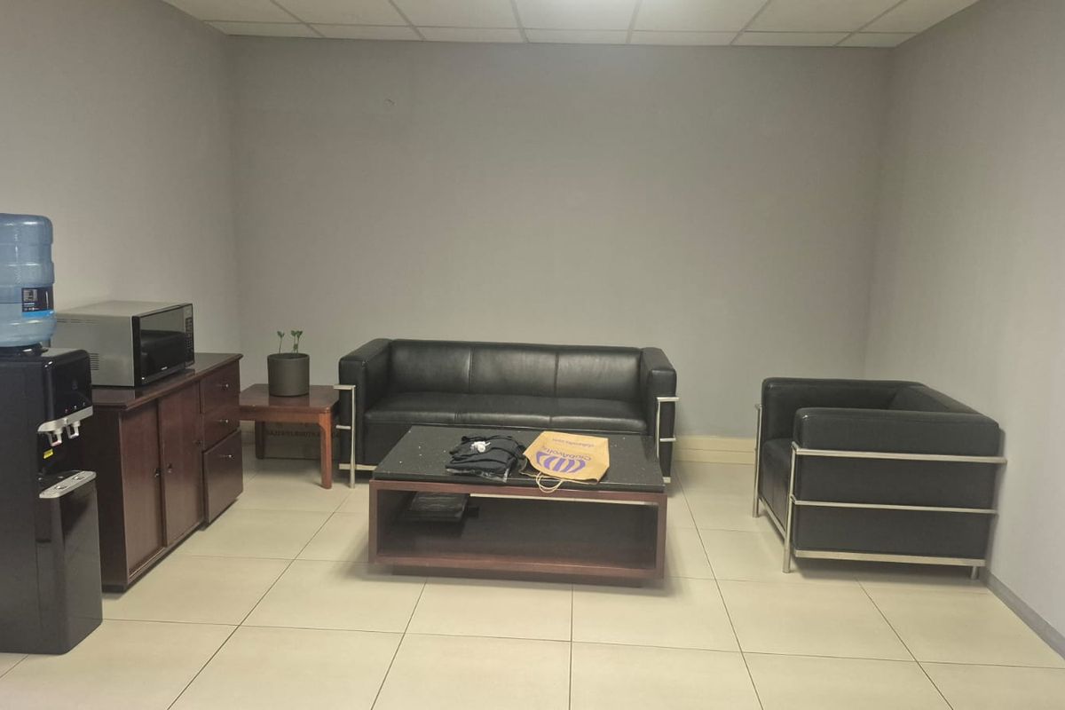 A functional office lounge or waiting area featuring neutral wall finishes, tiled flooring, and a suspended ceiling.