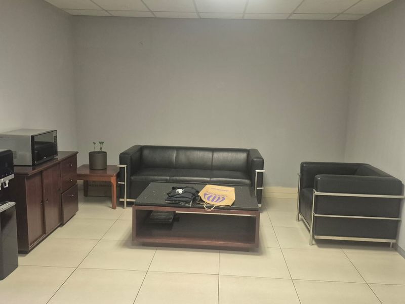 A functional office lounge or waiting area featuring neutral wall finishes, tiled flooring, and a suspended ceiling.