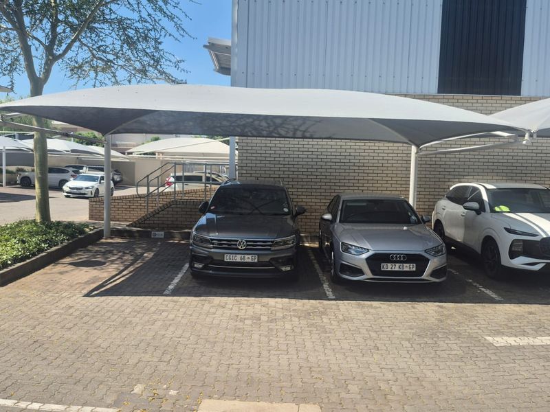 Industrial property exterior featuring a paved parking area with covered shade cloth carports and brick and metal building facade.