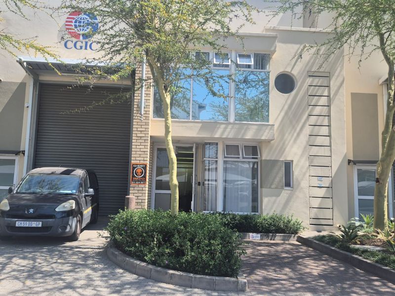 Front elevation of an industrial unit featuring a large roller shutter door, glass office frontage, and paved driveway access.