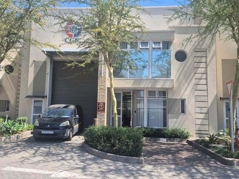 Front elevation of an industrial unit featuring a roller shutter door, paved driveway, and modern facade with aluminum window frames.