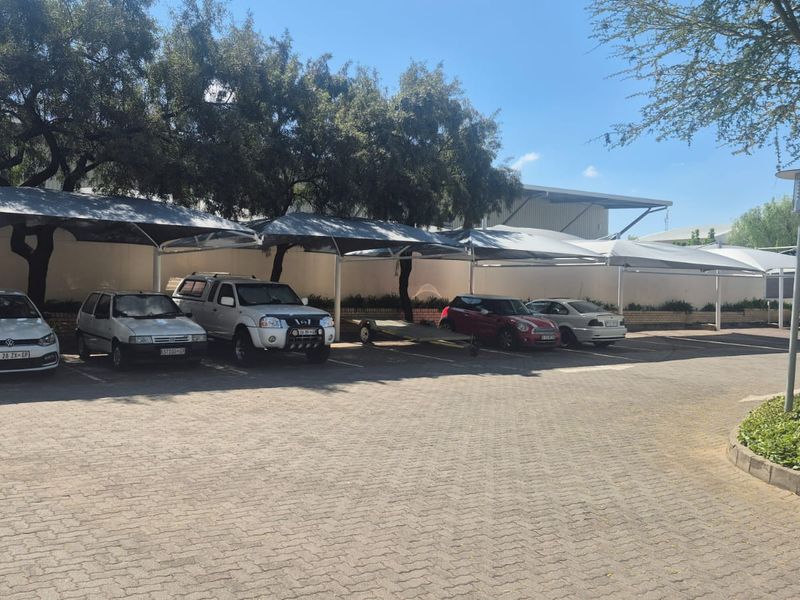 Industrial property exterior featuring a paved parking area with multiple shade cloth carports and established perimeter landscaping.