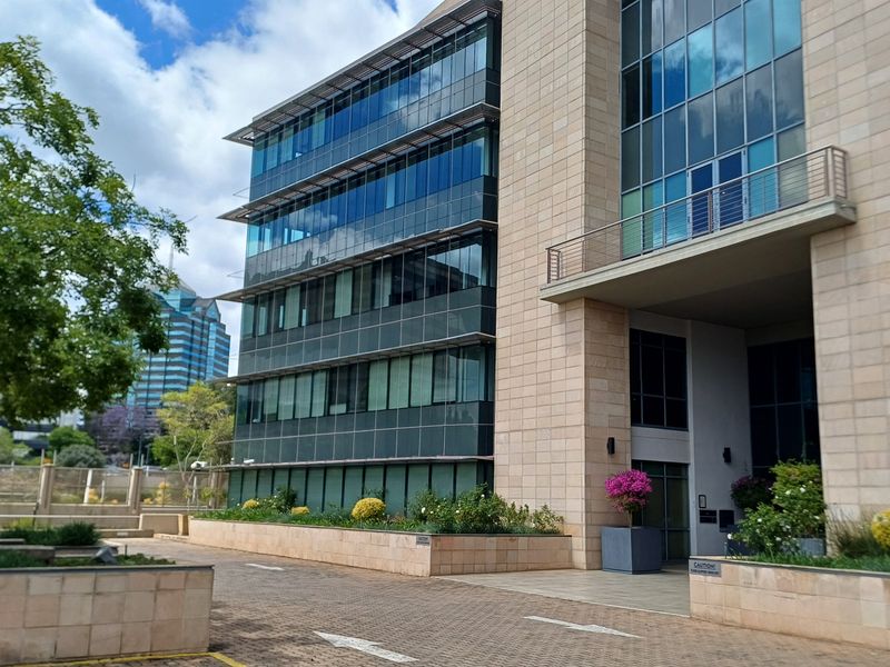 Modern multi-story commercial office building featuring a glass curtain wall facade, stone cladding, and a paved entrance area.