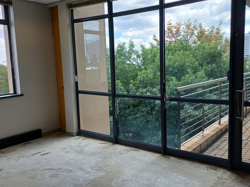 An empty office space featuring large windows and sliding doors leading to a balcony with metal railings and views.