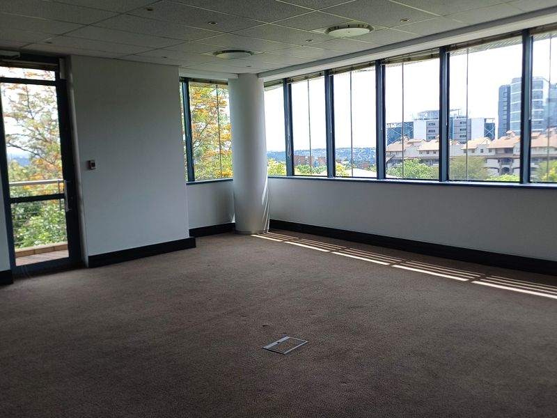 Spacious, empty office suite featuring large windows with city views, carpeted flooring, and integrated floor power outlets.