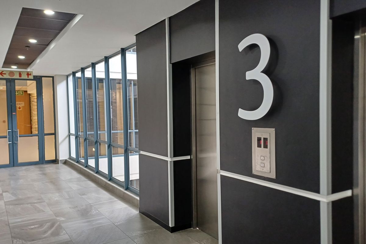 A modern, well-maintained commercial hallway featuring tiled flooring, large glass windows, and a clearly marked elevator access point on the third floor.