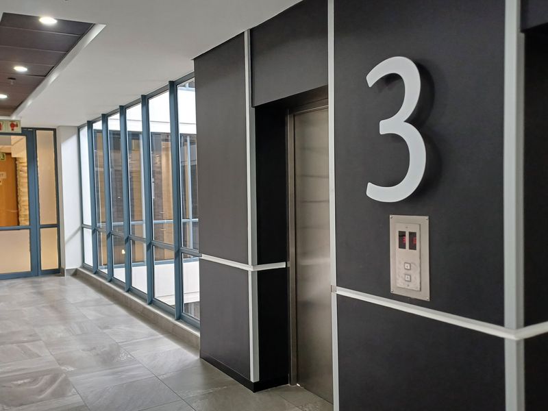 A modern, well-maintained commercial hallway featuring tiled flooring, large glass windows, and a clearly marked elevator access point on the third floor.
