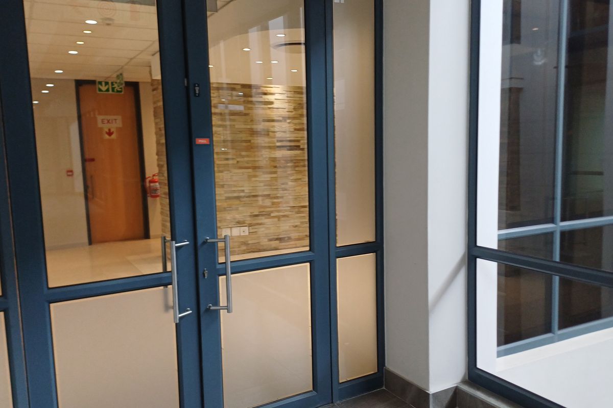 A modern commercial entrance featuring glass double doors, a stone feature wall, and recessed lighting in a clean, professional office environment.