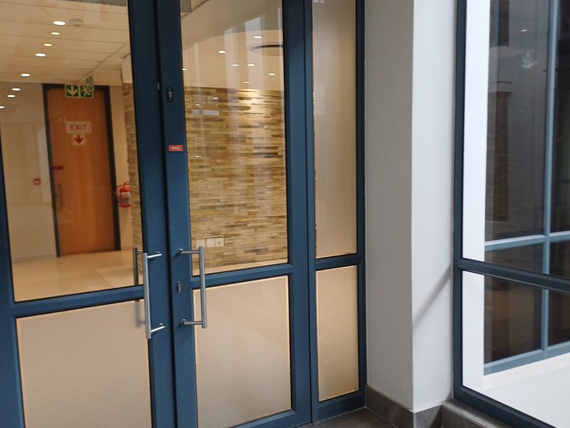A modern commercial entrance featuring glass double doors, a stone feature wall, and recessed lighting in a clean, professional office environment.