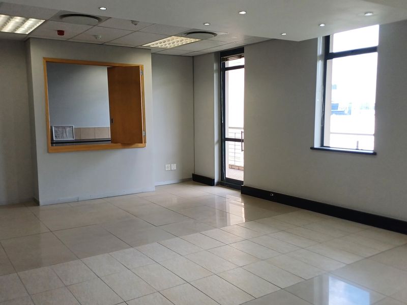 A bright, open-plan office space featuring tiled flooring, recessed ceiling lighting, and an internal service window, providing a clean and professional work environment.