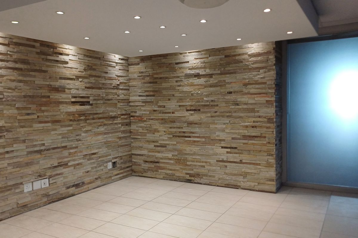 A modern office space featuring a decorative stacked stone feature wall, recessed ceiling lighting, and neutral tiled flooring with a frosted glass entrance.