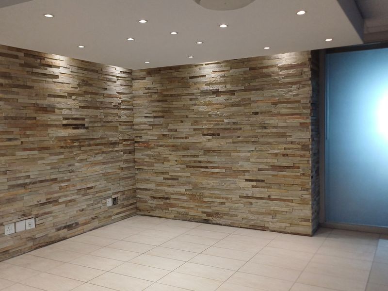 A modern office space featuring a decorative stacked stone feature wall, recessed ceiling lighting, and neutral tiled flooring with a frosted glass entrance.