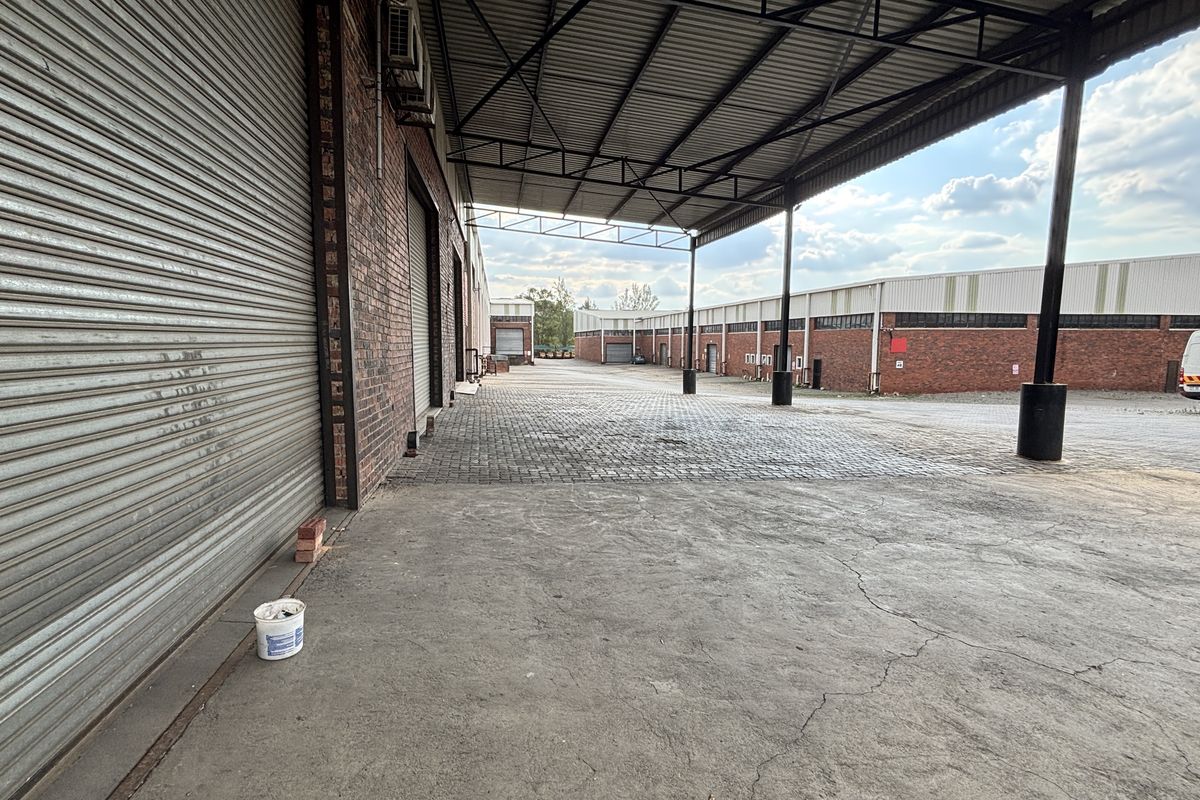 Spacious industrial loading area featuring a covered bay, roller shutter doors, and durable paved and concrete surfaces.