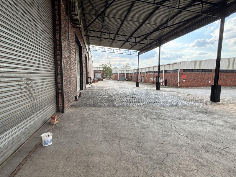 Spacious industrial loading area featuring a covered bay, roller shutter doors, and durable paved and concrete surfaces.