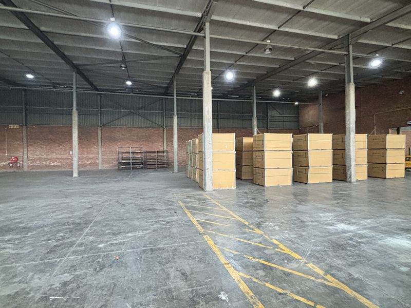 Spacious industrial warehouse featuring high ceilings, exposed steel trusses, concrete flooring, and brick wall construction, suitable for storage or manufacturing operations.