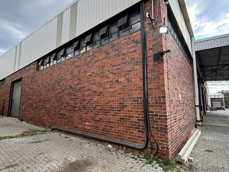 Exterior view of an industrial warehouse featuring face brick walls, corrugated metal cladding, high-level hopper windows, and a covered loading area with paved yard.