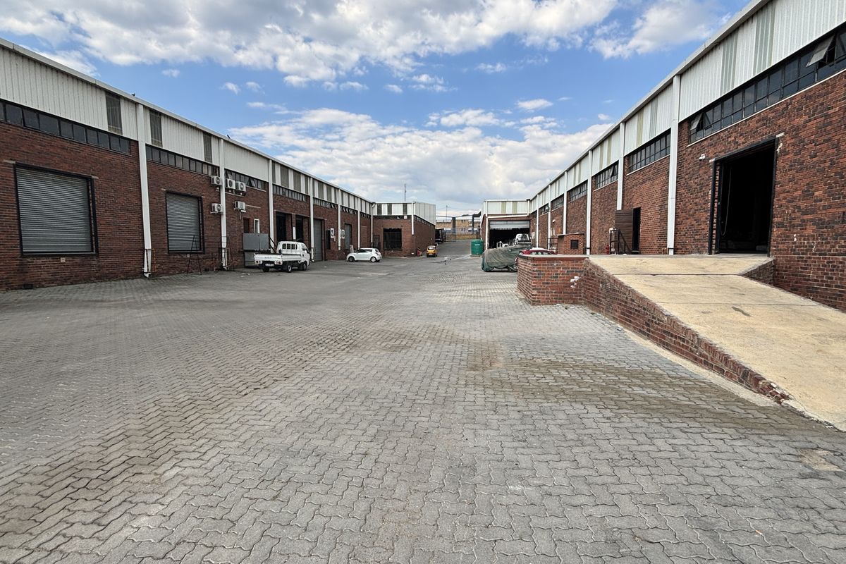 Spacious industrial yard featuring brick facades, multiple roller shutter doors, and a concrete loading ramp, providing functional access for logistics and operations.