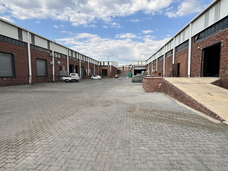 Spacious industrial yard featuring brick facades, multiple roller shutter doors, and a concrete loading ramp, providing functional access for logistics and operations.