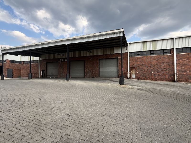 Industrial warehouse exterior featuring a large paved yard, covered loading area, and multiple roller shutter doors for efficient logistics and access.