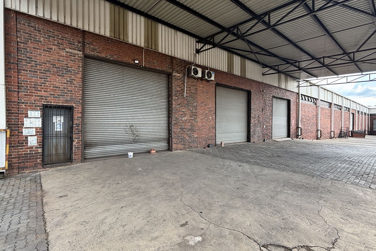 Industrial warehouse exterior featuring multiple roller shutter doors, a covered loading bay, and durable brick construction with paved access area.