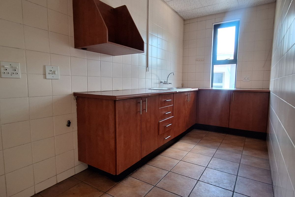 A functional office kitchenette featuring tiled walls, laminate cabinetry, and a stainless steel sink, providing a clean and practical utility space.