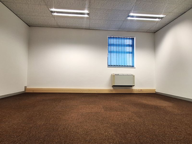 A vacant office space featuring carpet flooring, a suspended ceiling with integrated lighting, and a wall-mounted air conditioning unit.