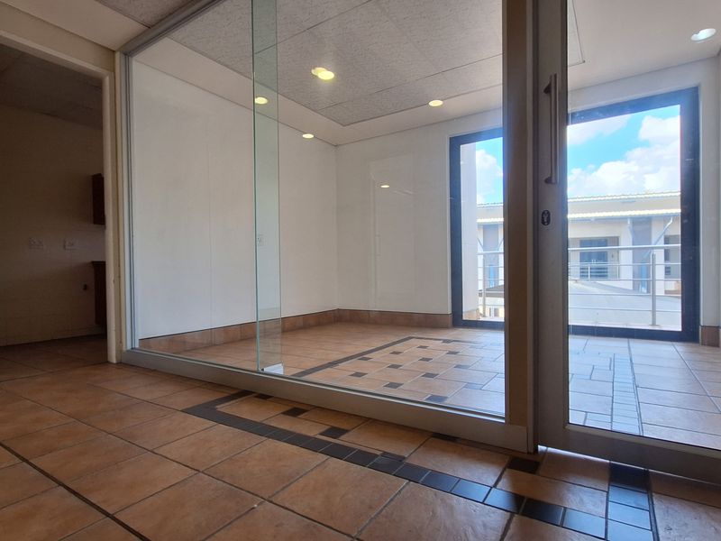 A bright, empty office space featuring glass partitioning, tiled flooring, and recessed lighting, offering a clean and professional environment for business operations.