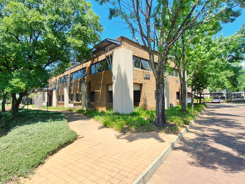 Exterior view of a multi-story brick office building featuring paved walkways, landscaped surroundings, and ample parking space in a professional office park setting.