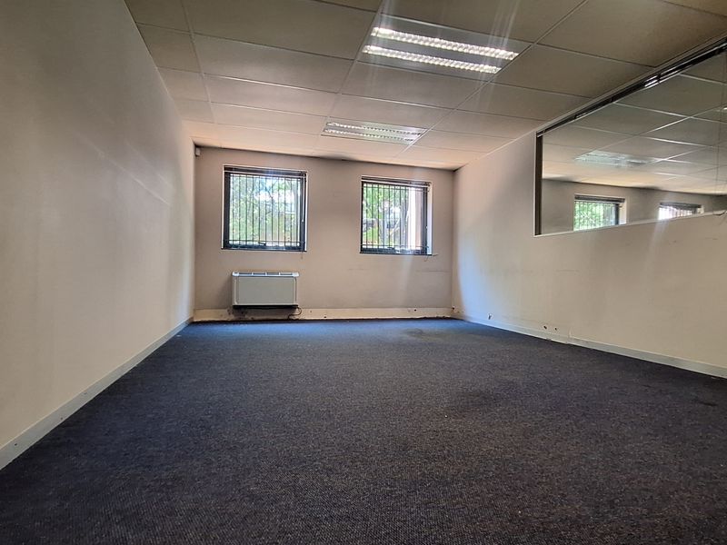An empty office space featuring a suspended ceiling, recessed lighting, wall-mounted air conditioning, and security bars on the windows.