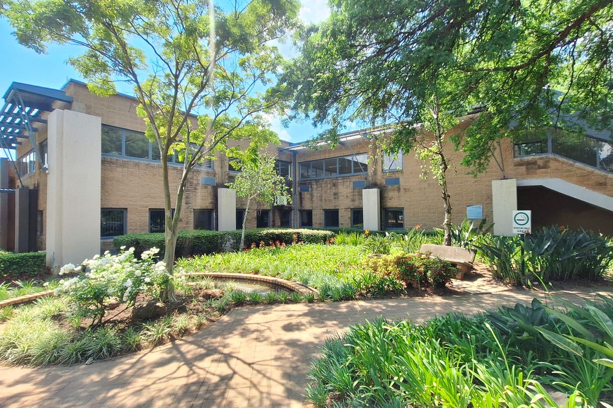 A well-maintained office building exterior featuring a brick facade, landscaped garden, paved walkways, and an external staircase.