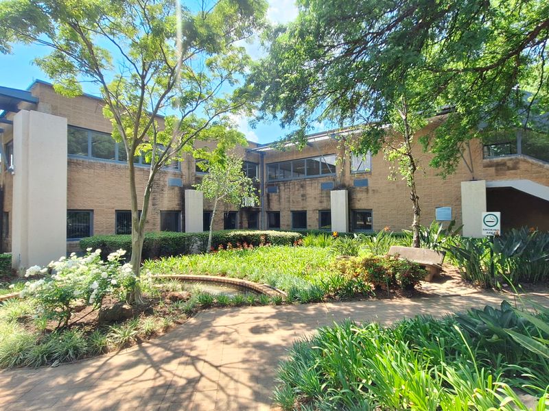 A well-maintained office building exterior featuring a brick facade, landscaped garden, paved walkways, and an external staircase.