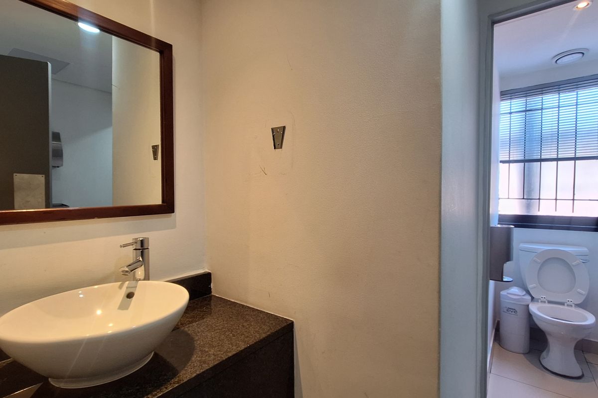 A functional office bathroom featuring a vessel sink on a granite vanity and a separate toilet area with natural light.