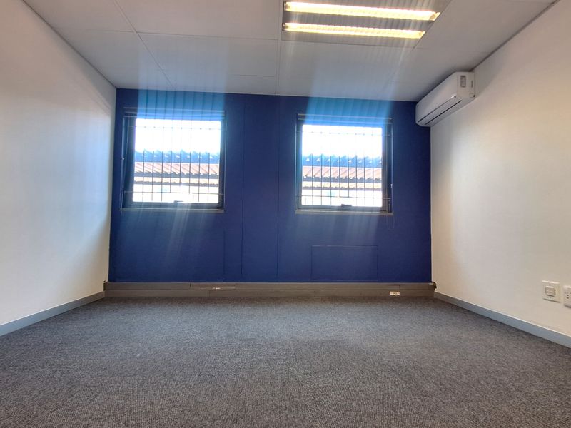 A clean, empty office space featuring carpeted flooring, air conditioning, and dual windows with security bars, suitable for a professional workspace.