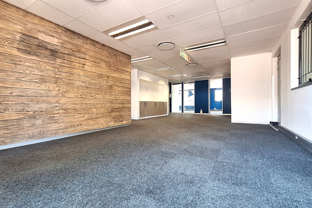A spacious, empty office area featuring a wood-paneled accent wall, recessed lighting, built-in cabinetry, and carpeted flooring.
