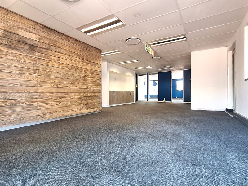 A spacious, empty office area featuring a wood-paneled accent wall, recessed lighting, built-in cabinetry, and carpeted flooring.