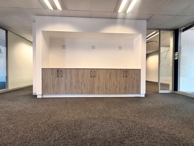 A modern, empty office space featuring built-in wood-finish cabinetry, carpeted flooring, and glass partition walls, providing a clean and professional work environment.