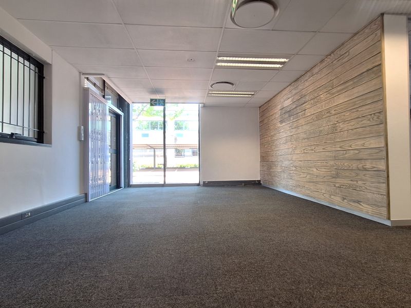 A bright, open-plan office space featuring carpeted flooring, a modern timber-look feature wall, and recessed ceiling lighting with secure access points.