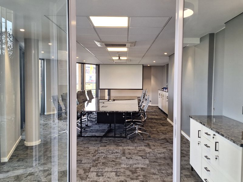 A modern, professional office boardroom featuring glass partitions, built-in storage cabinetry, recessed lighting, and a projector screen, finished with high-quality carpeting.