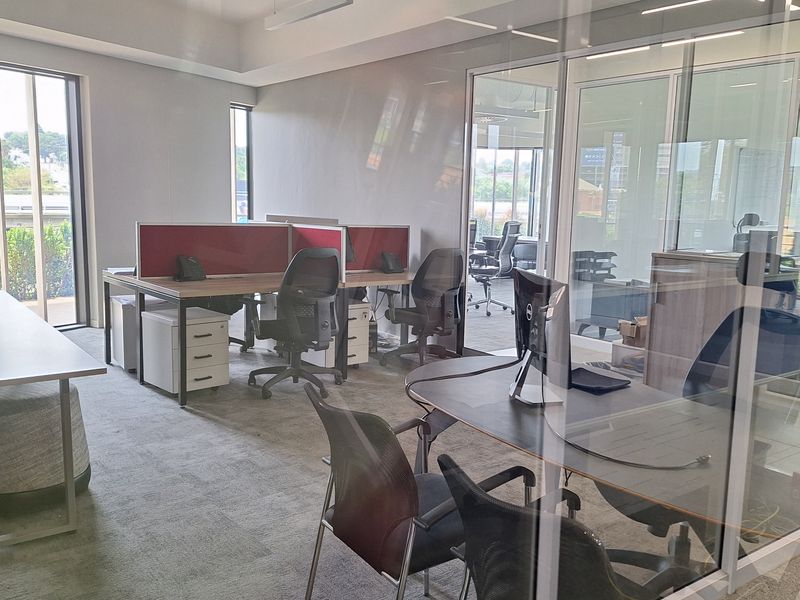 Modern professional office space featuring glass partition walls, recessed ceiling lighting, integrated air conditioning, and carpeted flooring with ample natural light.
