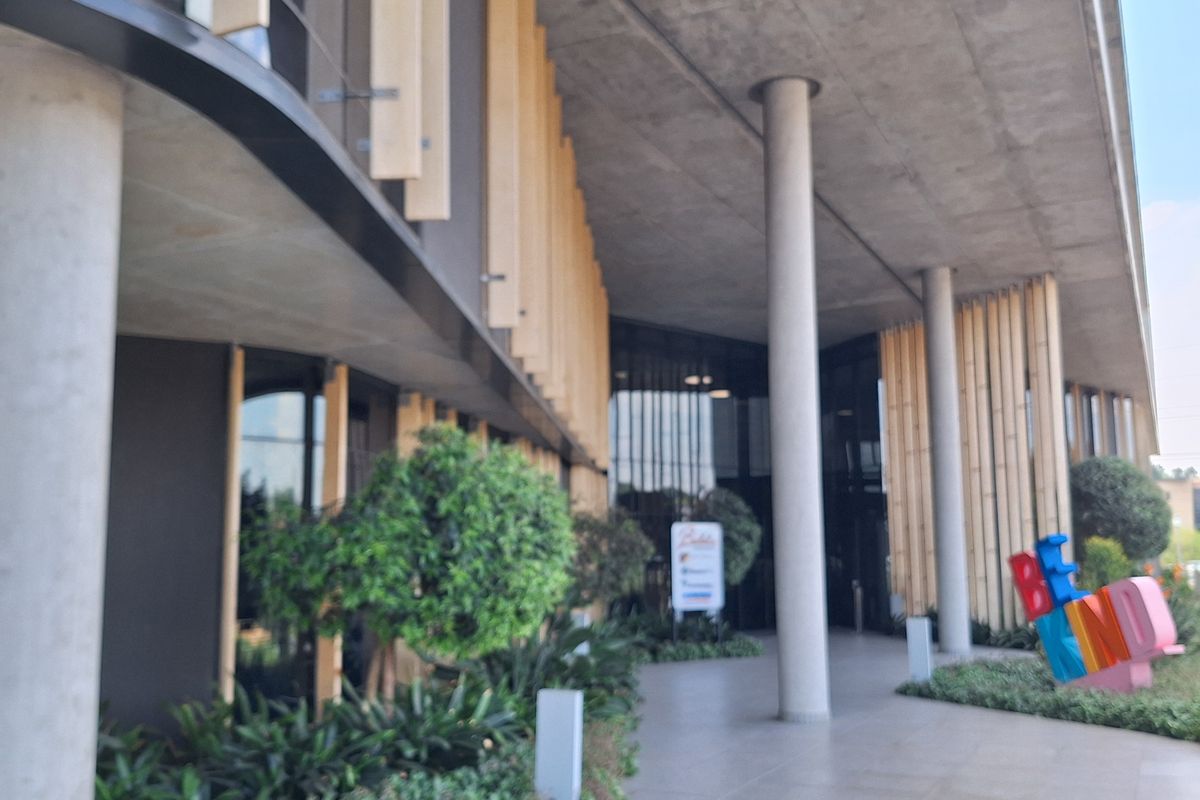 Modern office building entrance featuring a covered walkway with concrete columns, tiled flooring, and a contemporary glass facade with timber accents.