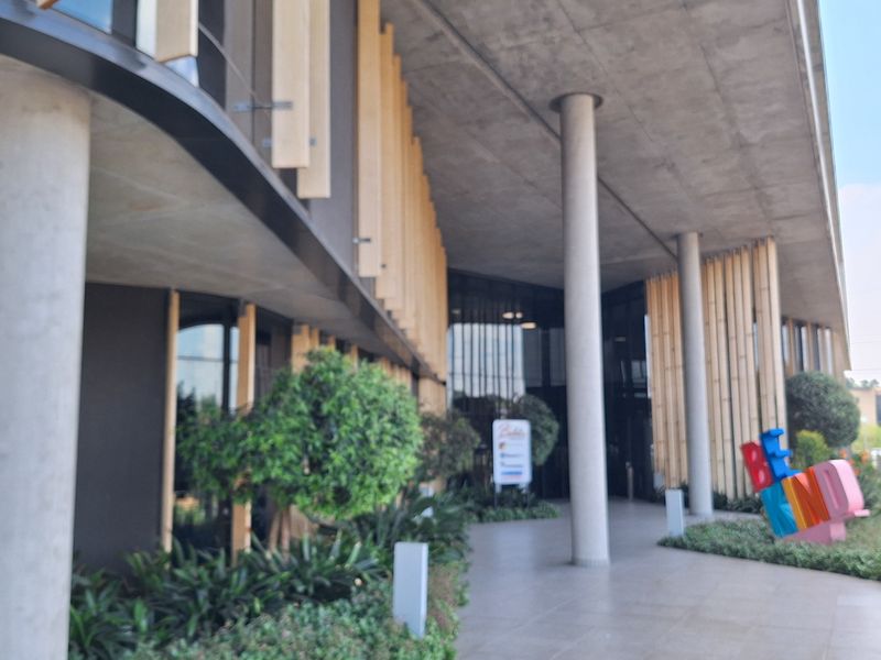 Modern office building entrance featuring a covered walkway with concrete columns, tiled flooring, and a contemporary glass facade with timber accents.