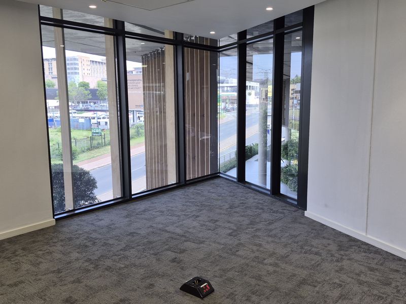 A bright, modern, empty office space featuring floor-to-ceiling windows with corner views, recessed lighting, and neutral carpeted flooring.