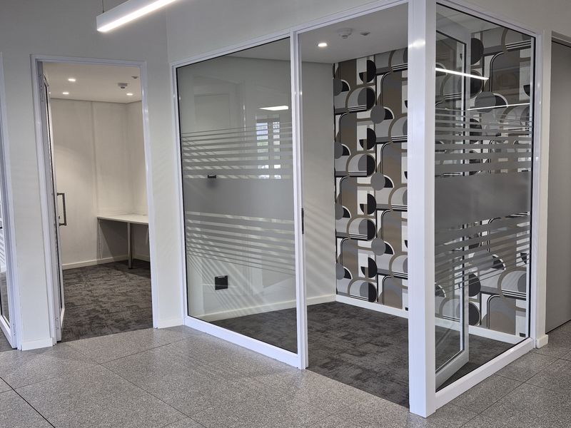 Modern office space featuring glass partition walls, recessed lighting, and a mix of carpet and tiled flooring in a professional commercial setting.