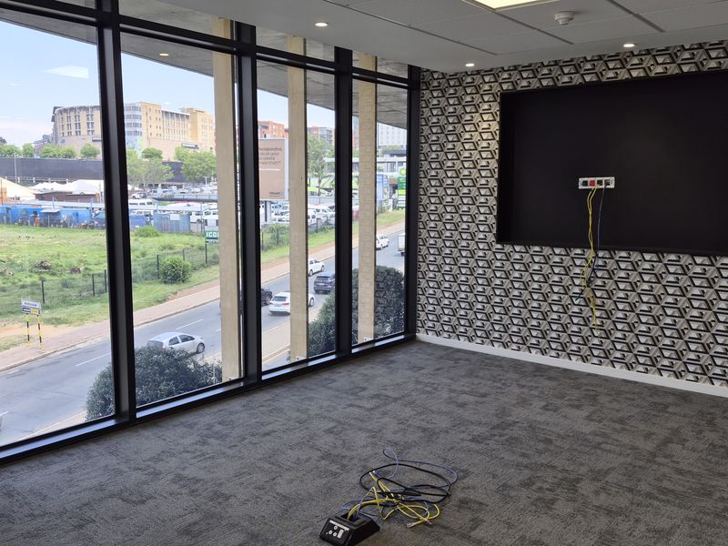 A vacant office space featuring floor-to-ceiling windows with urban views, patterned feature wall, recessed lighting, and carpeted flooring.