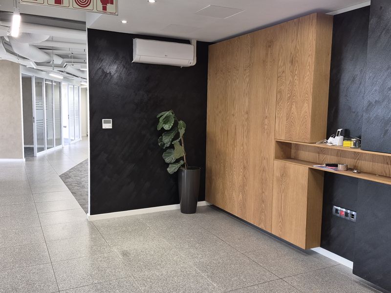 Modern office space featuring sleek black feature walls, integrated wood-grain cabinetry, tiled flooring, and glass partitions with efficient air conditioning.